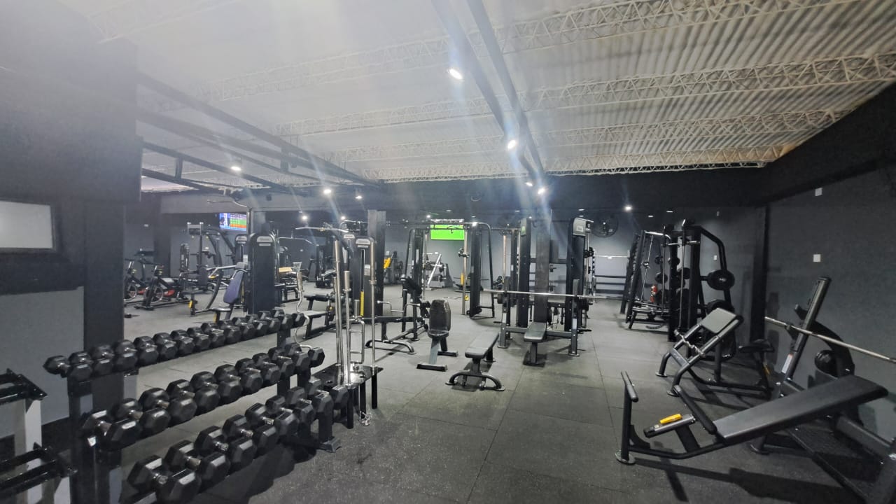 Zona de Fuerza y Pesas Libres de Oxigeno Gym con mancuernas alineadas y jaula de potencia
